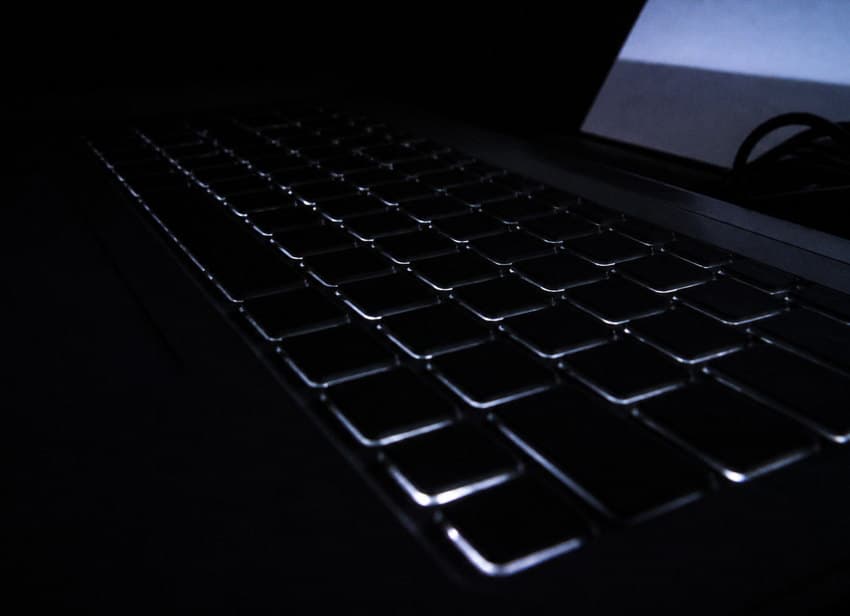 A laptop keyboard in a dark room, backlight glowing between the keys.