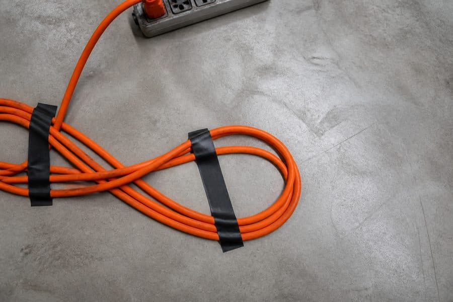 A bright orange extension cable coiled on a concrete floor, taped down with two strips of gaffer tape.