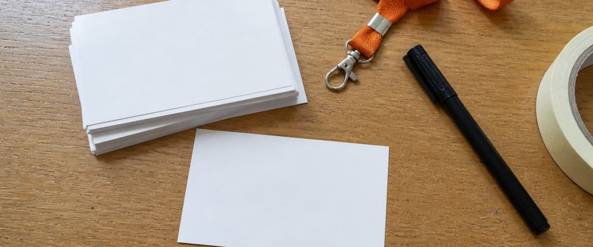 Blank badge cards, an orange lanyard, a marker and a roll of tape on a table, mid-preparation.